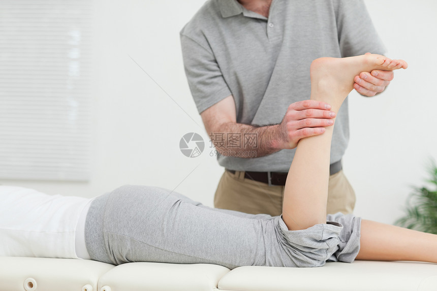 妇女躺在前方 而一名理疗师检查她的腿图片