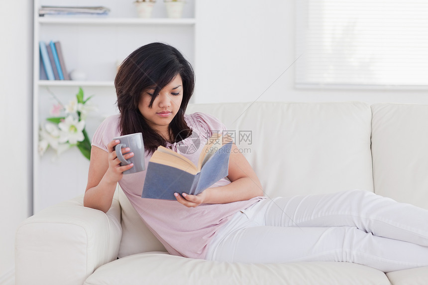 女人躺在沙发上 拿着杯子和书图片