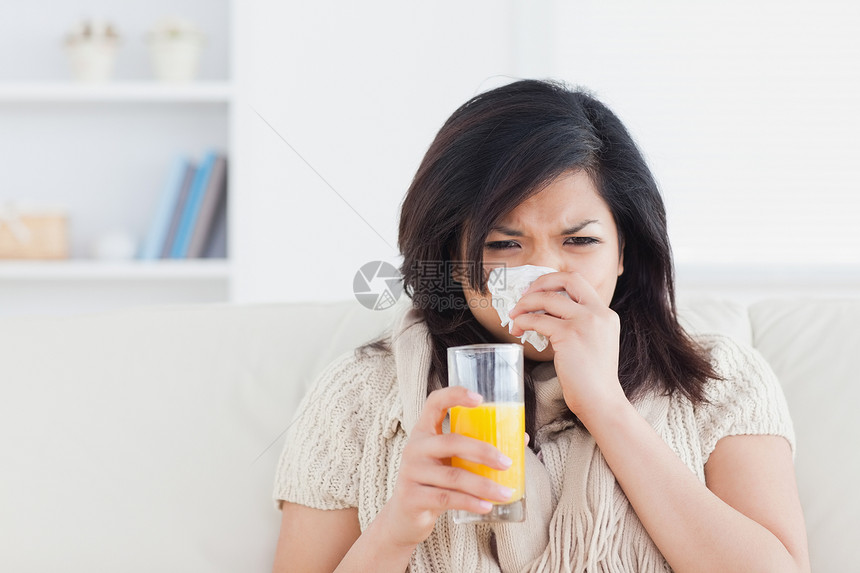 女人在打喷嚏时拿着一杯橙汁沙发组织杯子咖啡女性花朵橙子果汁棕色窗户图片