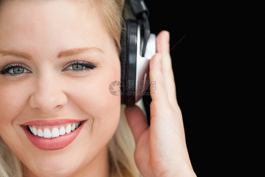 微笑的金发金发女人 通过耳机听音乐图片