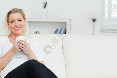 女人在沙发上喝咖啡牛仔裤女性休息室金发女郎巧克力金发划线白色浅色头发背景图片
