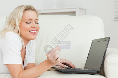 持有信用卡和笔记本电脑的妇女休息室浅色键盘电子商务屏幕客厅长椅沙发头发网站背景图片