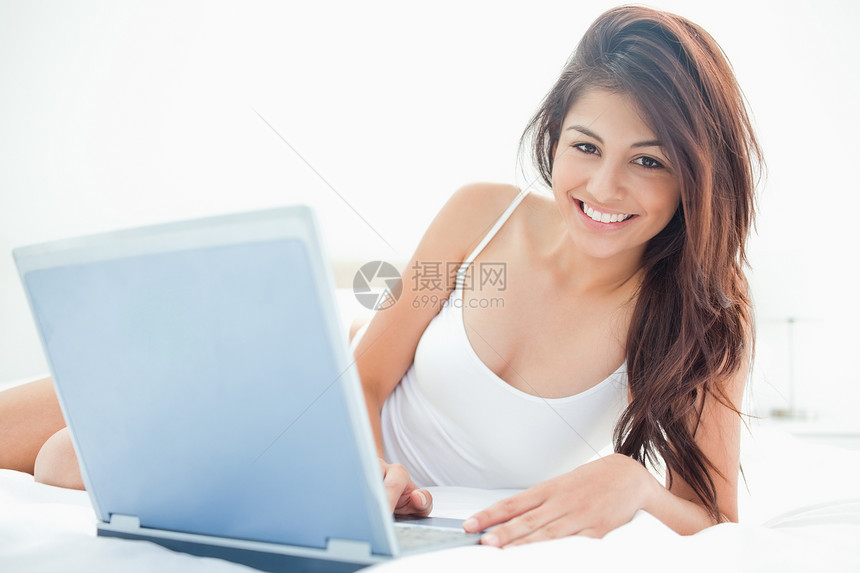 女人躺在床对面 她的笔记本电脑在她旁边图片