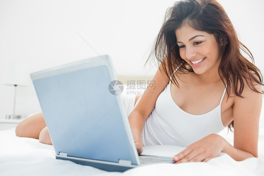 妇女躺在床上 用她的笔记本电脑享受着图片