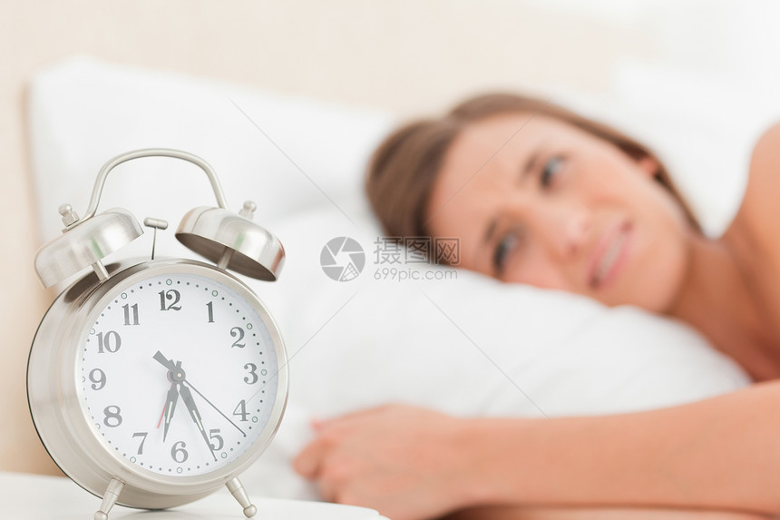 女人躺在床上 她的闹钟 在她展示时间旁边图片