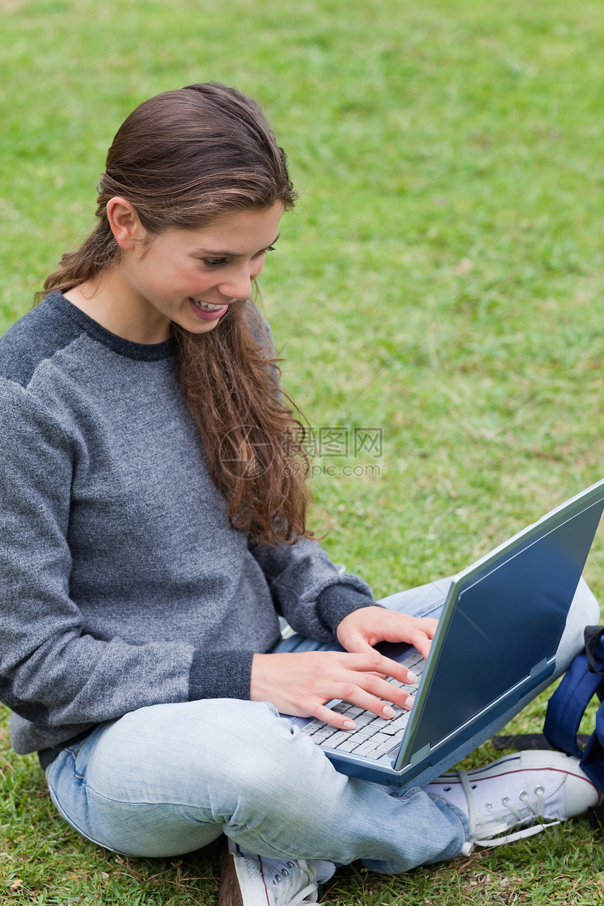 微笑的学生在她笔记本电脑上打字时坐在那里图片