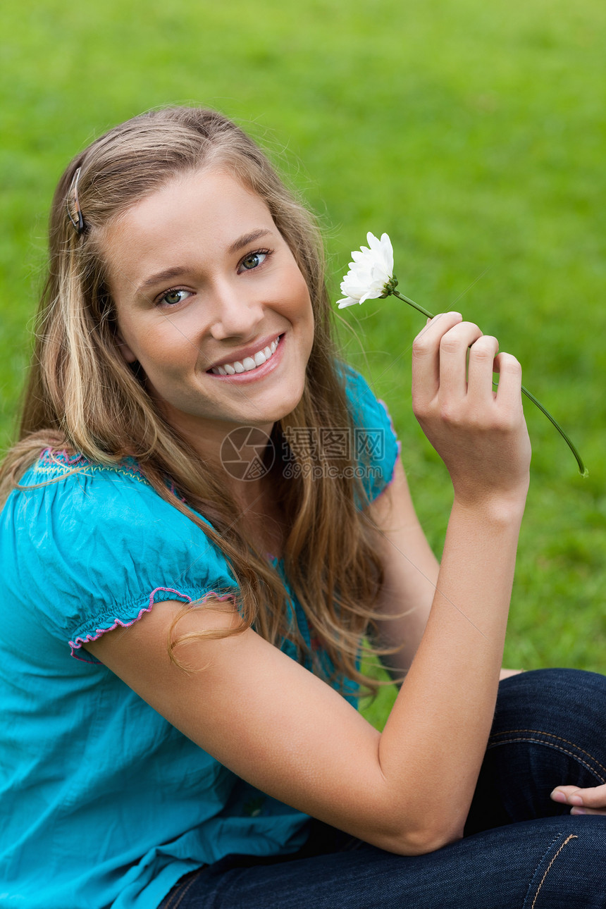 年轻笑容的女士 坐着时拿着花朵图片