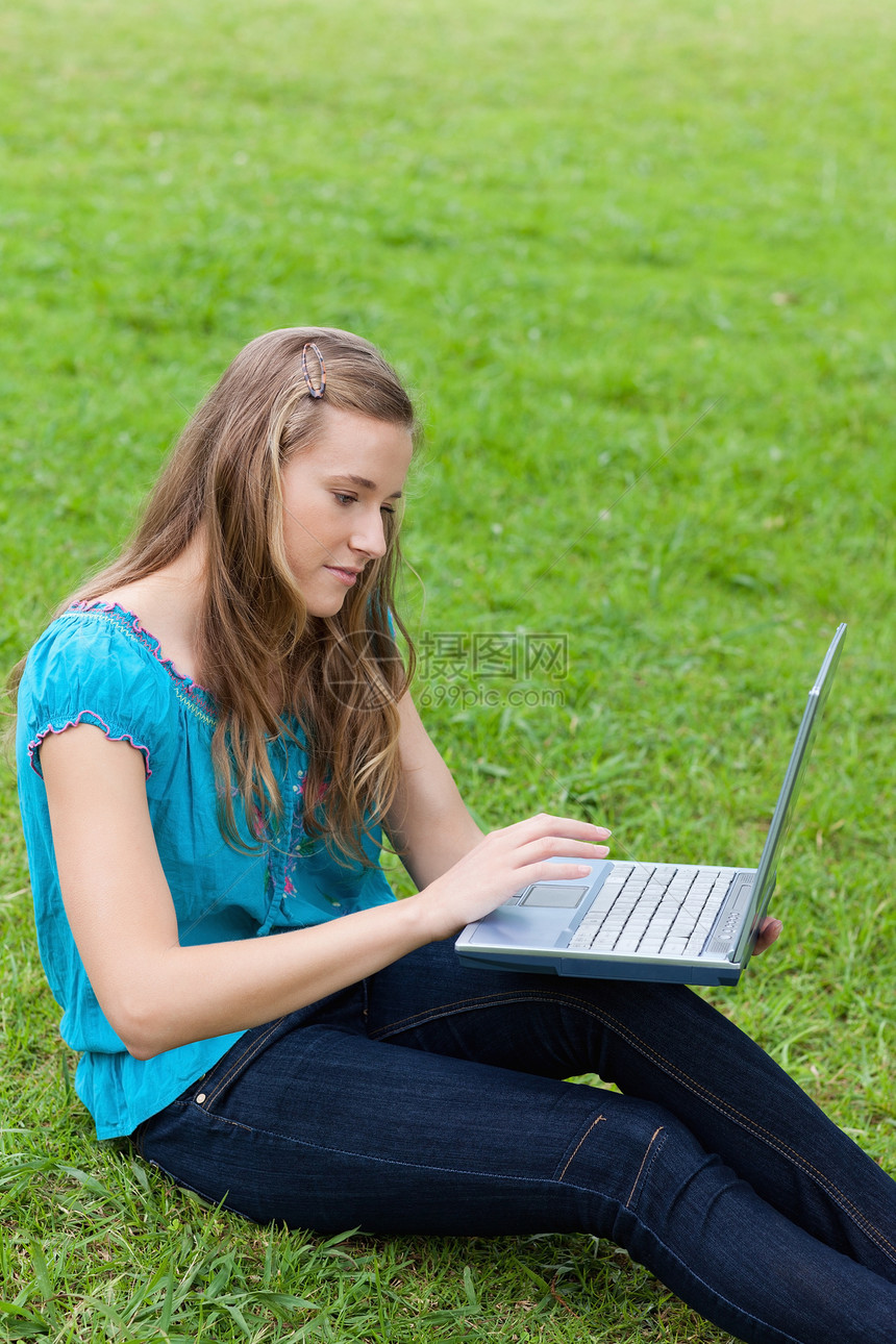 年轻放松的女人坐在草地上时使用笔记本电脑图片