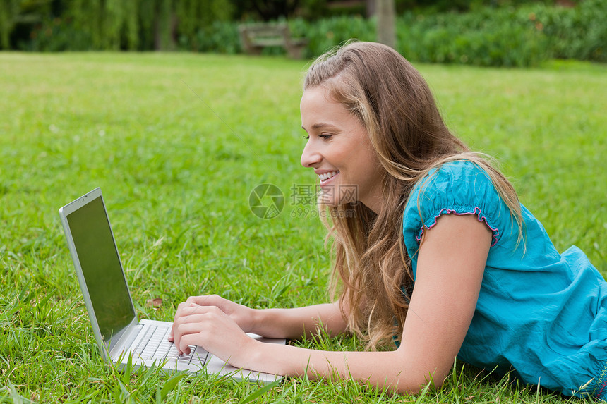 年轻微笑的女孩看着她的笔记本电脑 躺在地上图片
