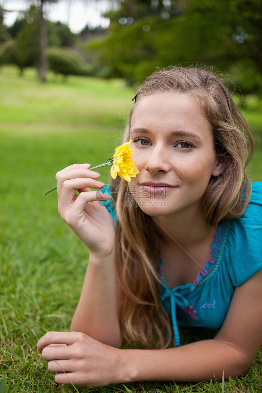 在公园里躺着时拿着黄色花朵的年轻放松女孩图片