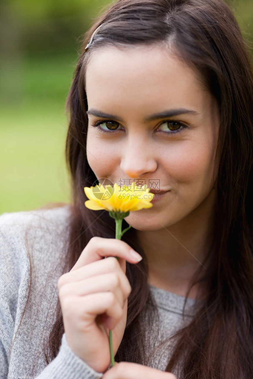 年轻女人一边看镜头 一边闻着黄色花朵的气味图片