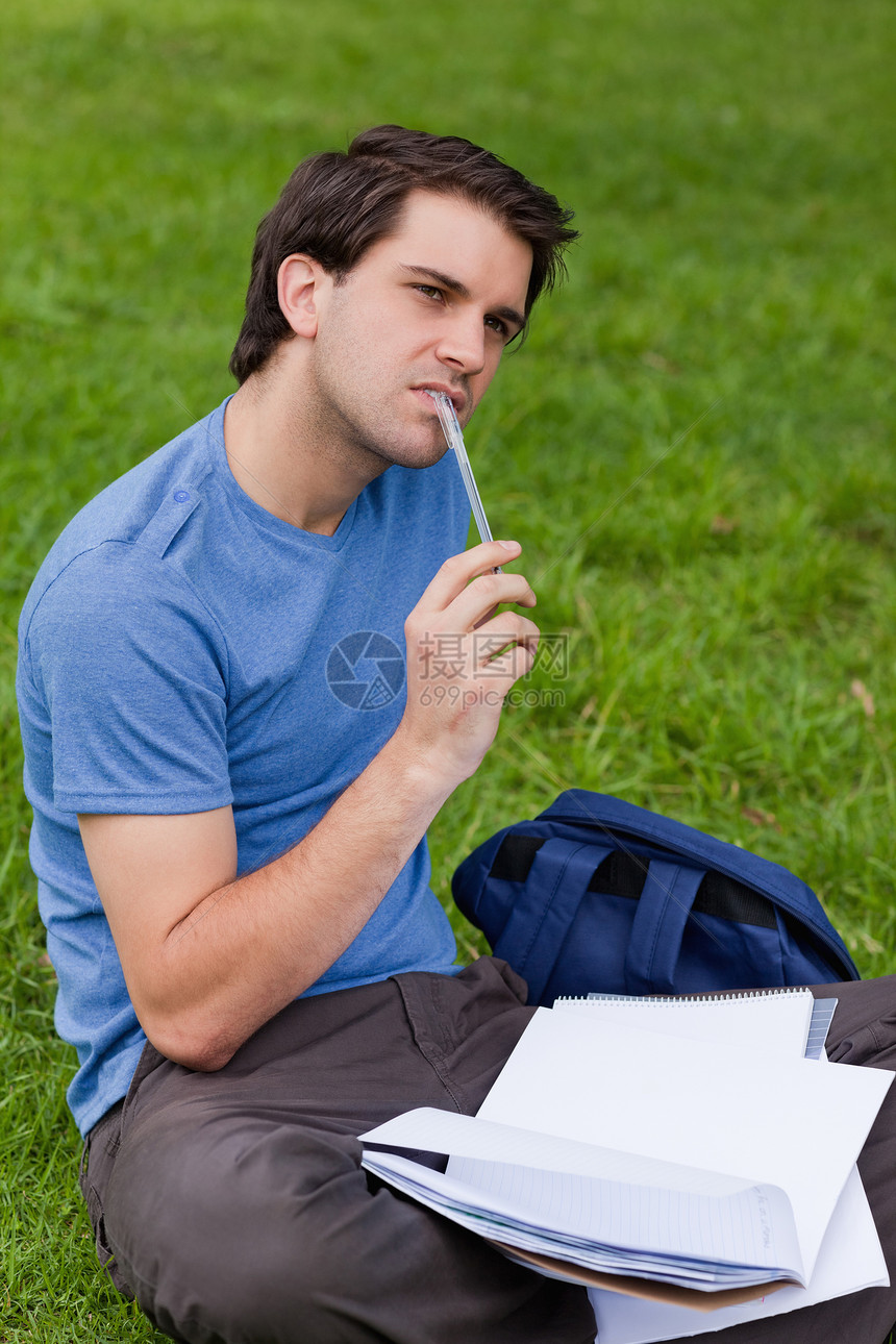 年轻有见识的人坐在草地上时拿着笔图片