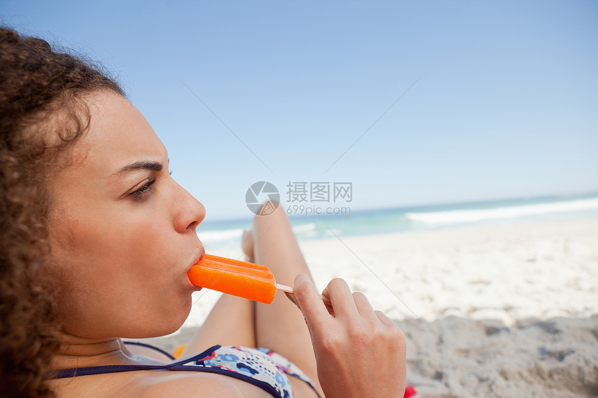 在海滩上吃冰棍的年轻有魅力的女人图片