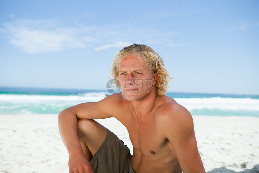 坐在沙滩上认真的男子 一边看着另一边图片