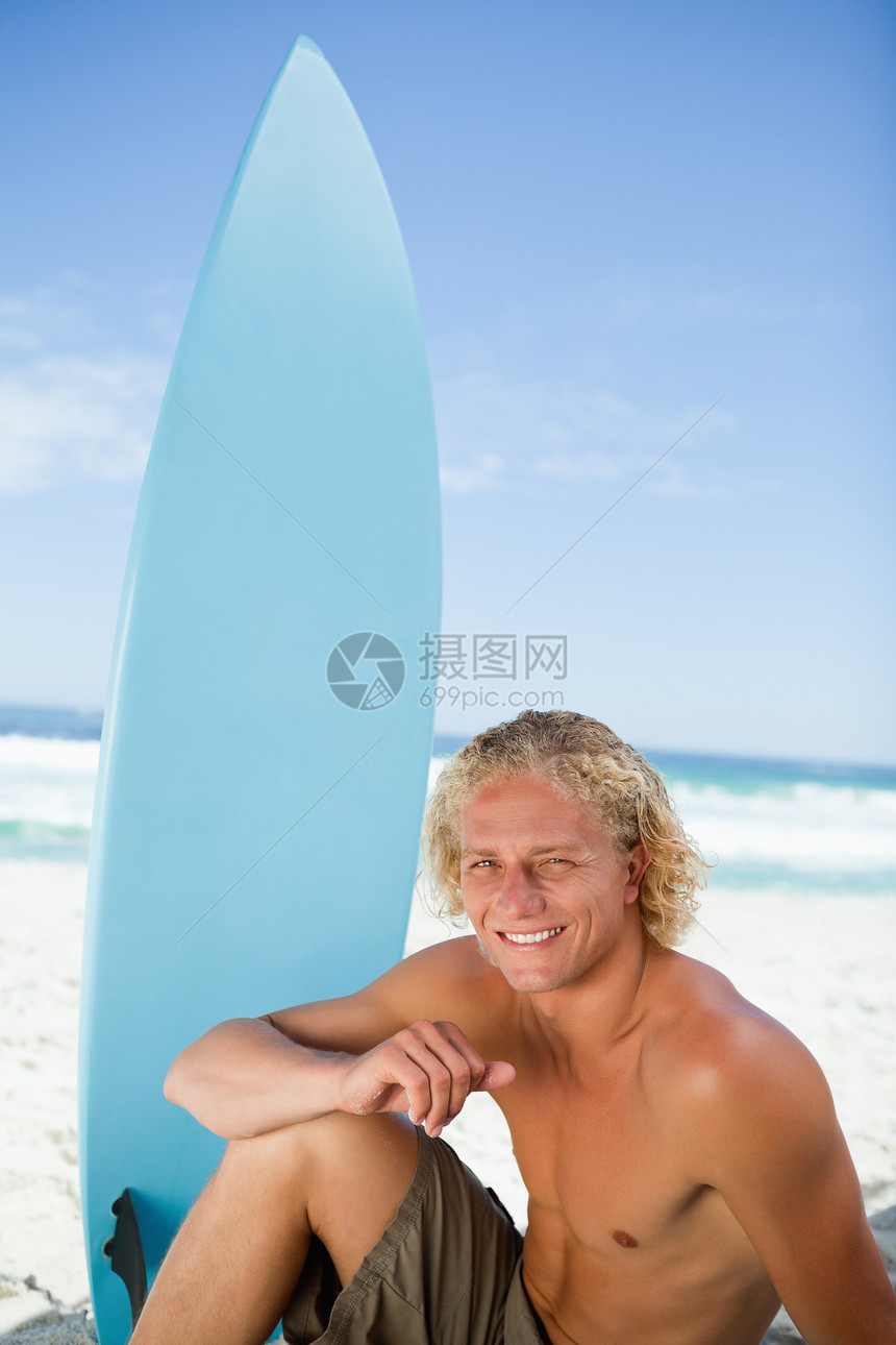 微笑的男人坐在沙滩上 他的手臂在腿上图片