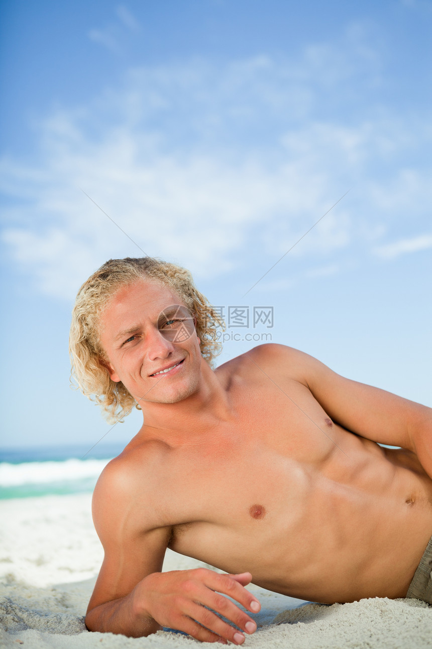 年轻微笑的男人躺在沙滩上 看着摄影机图片
