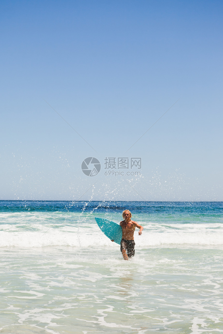 年轻金发金发男子 在跑步时回到海滩上图片