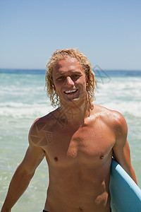 微笑的人站在水中 拿着冲浪板站着背景图片