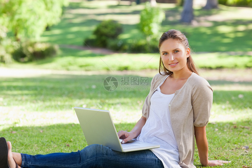 女人用笔记本电脑坐在草坪上绿色地面树叶森林阳光自由女士土地闲暇享受图片