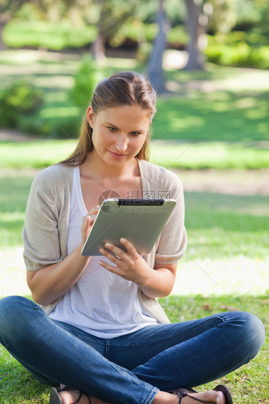 女人坐在草地上 同时使用平板电脑图片