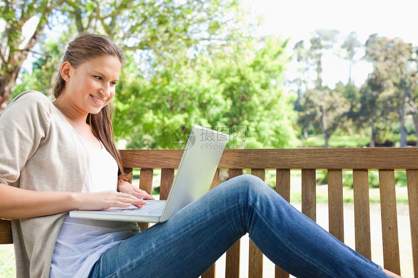 一个带着笔记本电脑坐在长椅上 微笑着的女人的侧面景色图片
