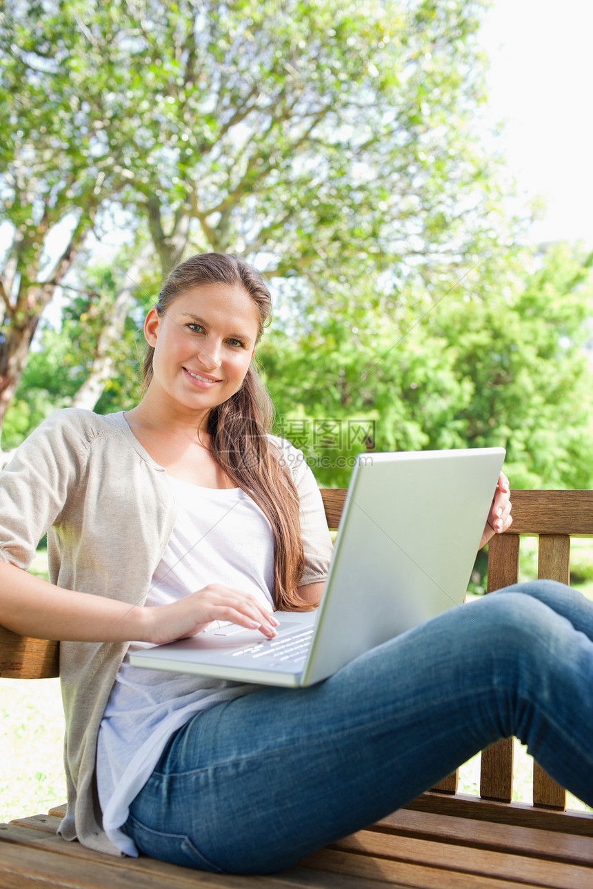 微笑的女人 用笔记本电脑坐在公园长椅上图片