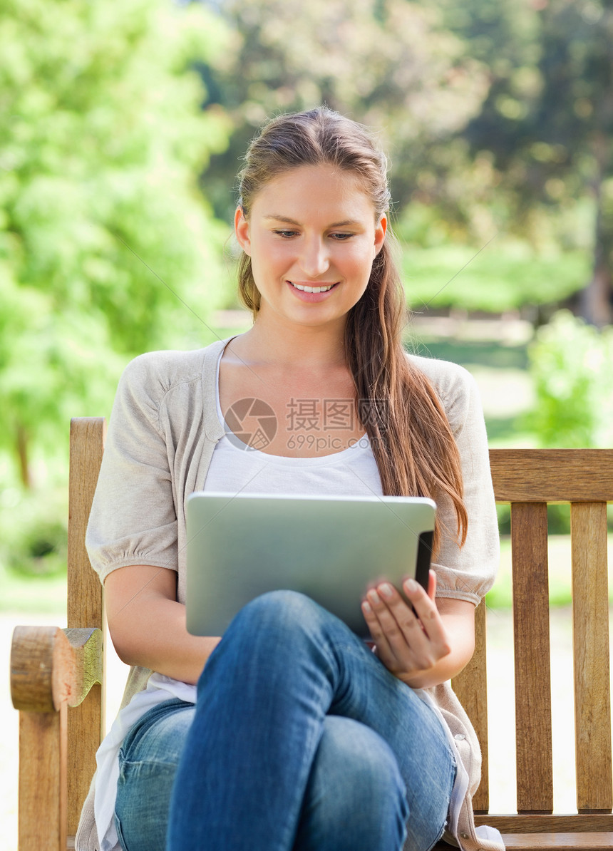 微笑的女人在公园长椅上使用平板电脑图片