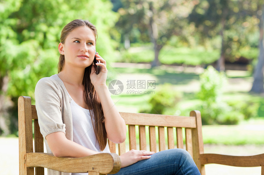 手机上的女人 在公园长椅上自由树叶闲暇女性喜悦森林草地阳光电话细胞图片