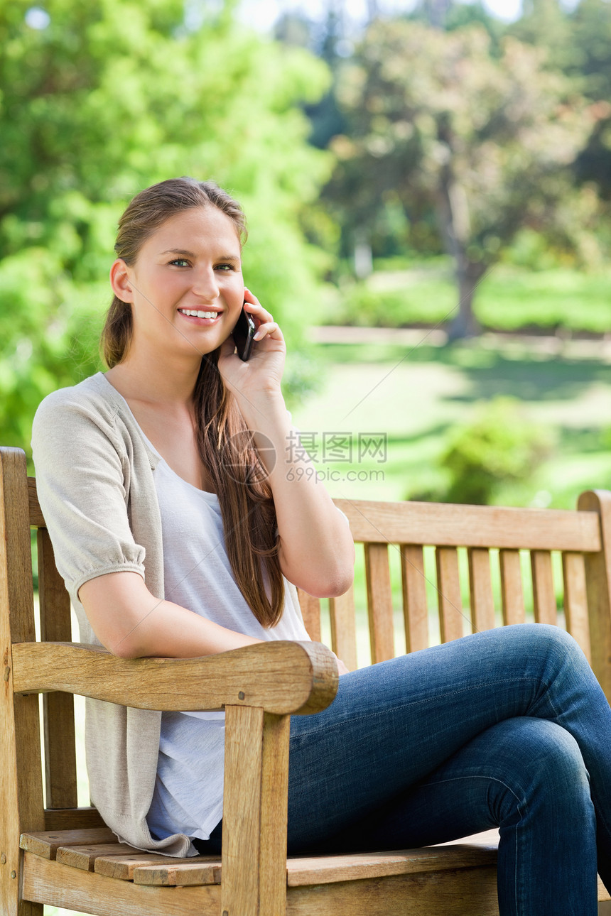 带着手机坐在公园长椅上的笑脸女人图片