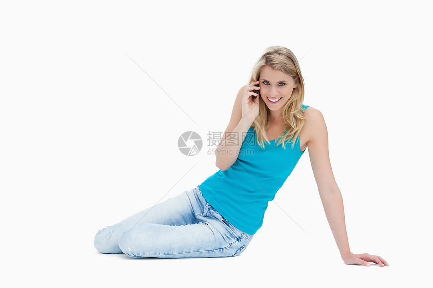 一个笑着的女人坐在地板上 说话在她的手机上图片