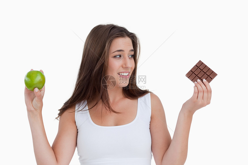 年轻黑发女人拿着一块巧克力和一个苹果图片