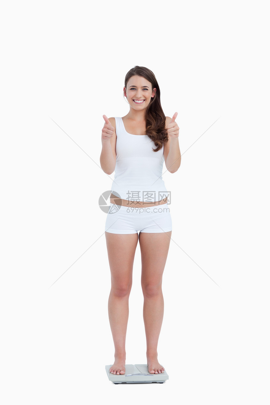 笑女人站着抬起拇指 站在体重上图片