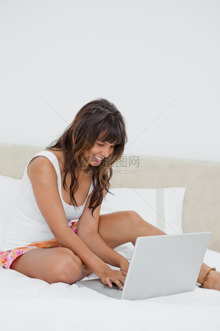 年轻妇女在笔记本电脑上聊天女性白色学生微笑外表睡衣卧室图片