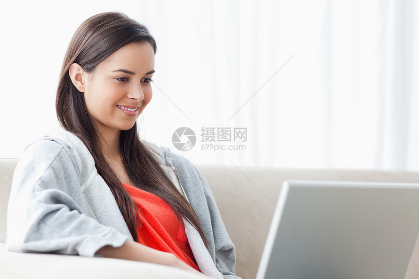 一个微笑的女人 在沙发上放松时 用她的笔记本电脑图片