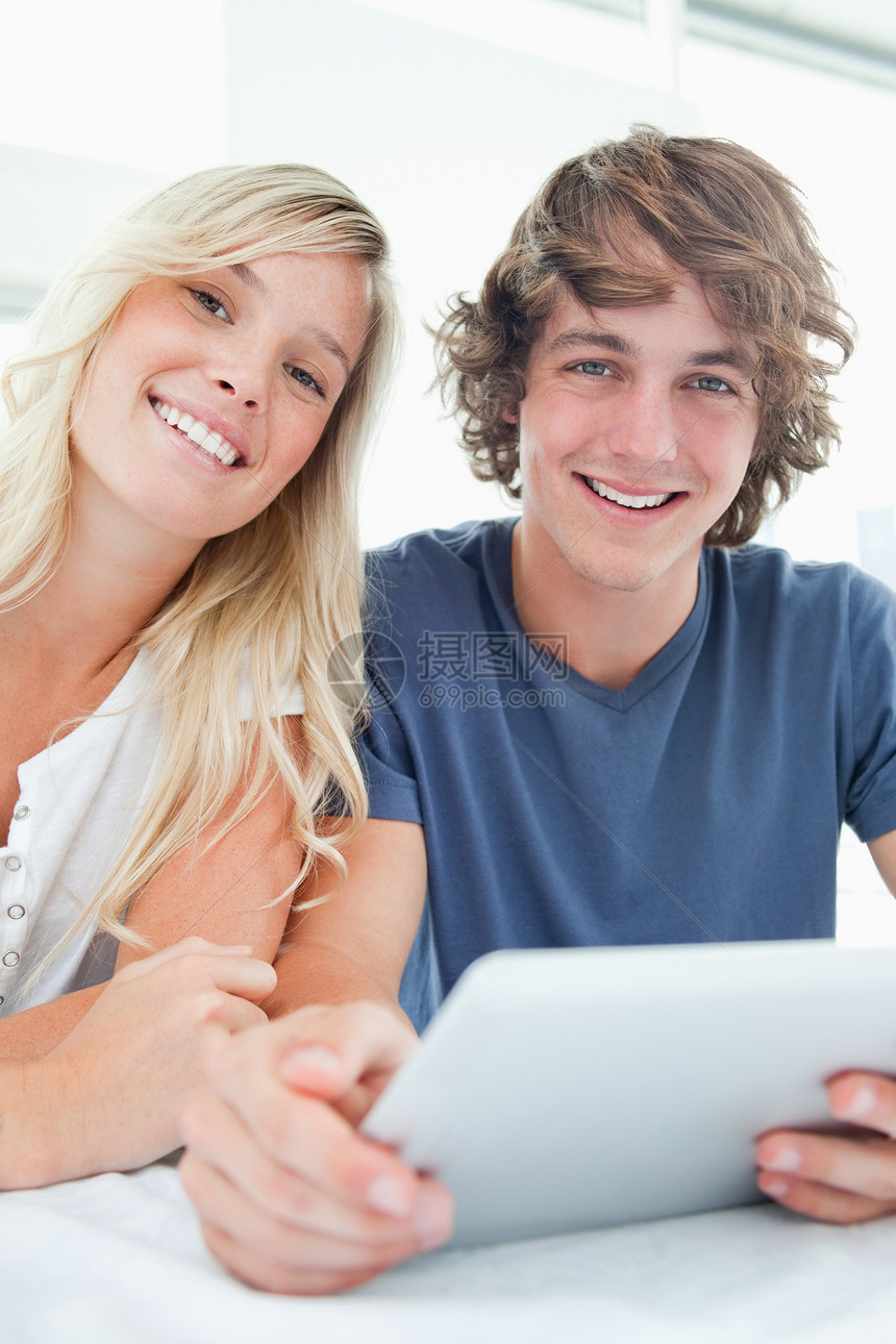 一对微笑的情侣拿着平板电脑看着相机快乐桌子药片成年人外表女性年轻人金发女郎图片