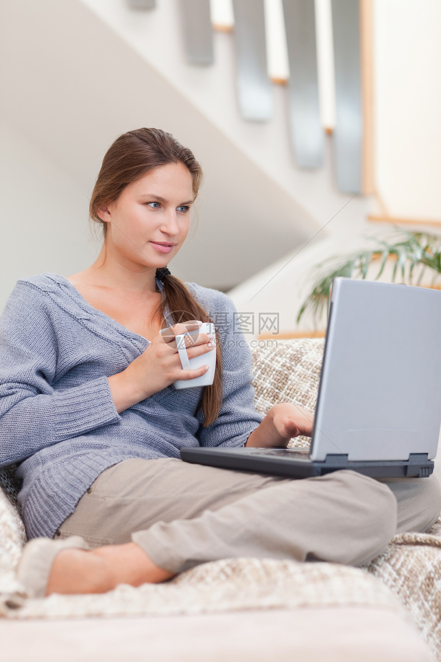 一个女人在喝茶时使用笔记本电脑的肖像闲暇互联网咖啡沙发饮料房子房间网络女性快乐图片