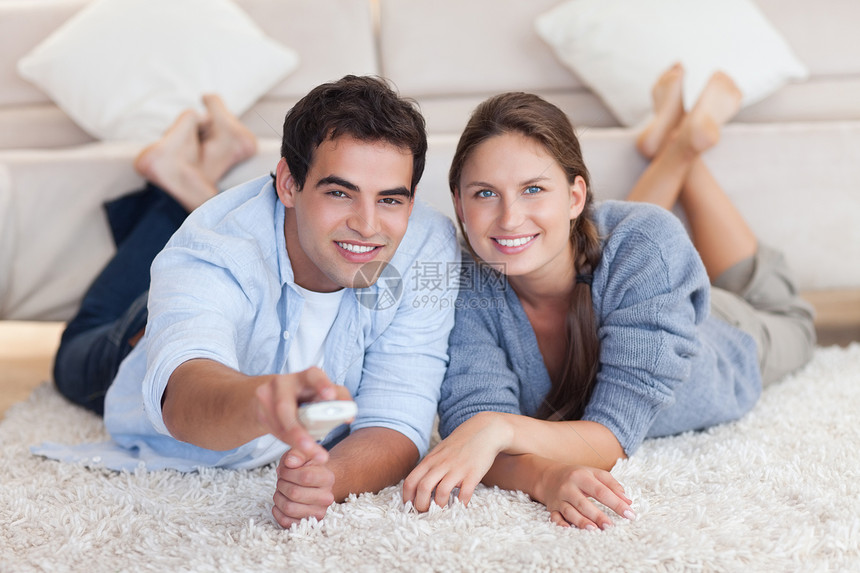 一对微笑的夫妇躺在地毯上看电视图片