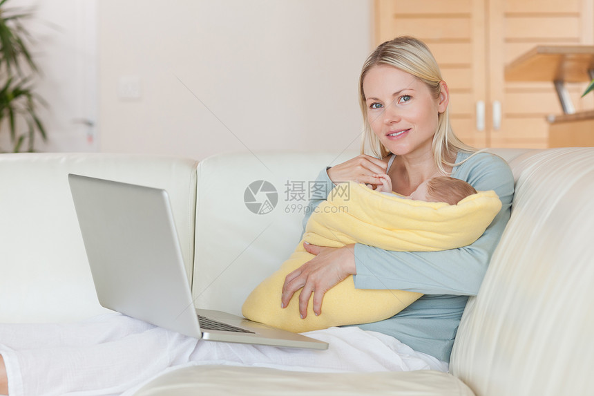 妈妈带着笔记本电脑在沙发上 抱着她的孩子客厅睡眠快乐拥抱团结女婴育儿幸福休息家庭图片