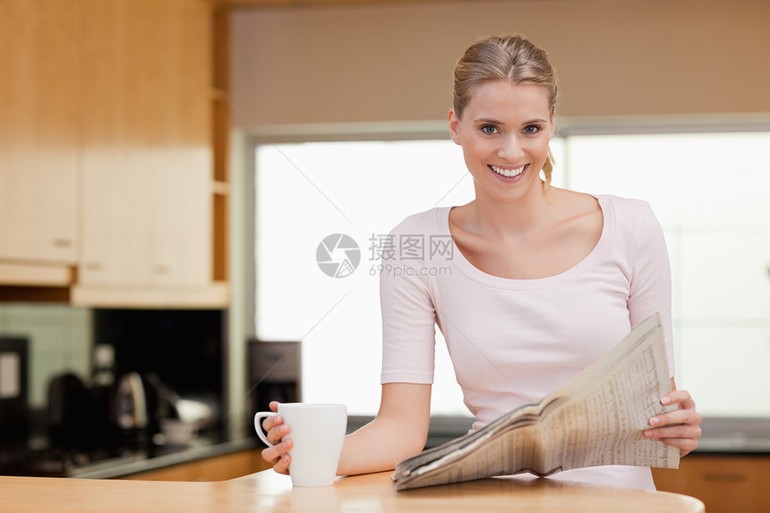 微笑的女人在喝茶时看新闻图片