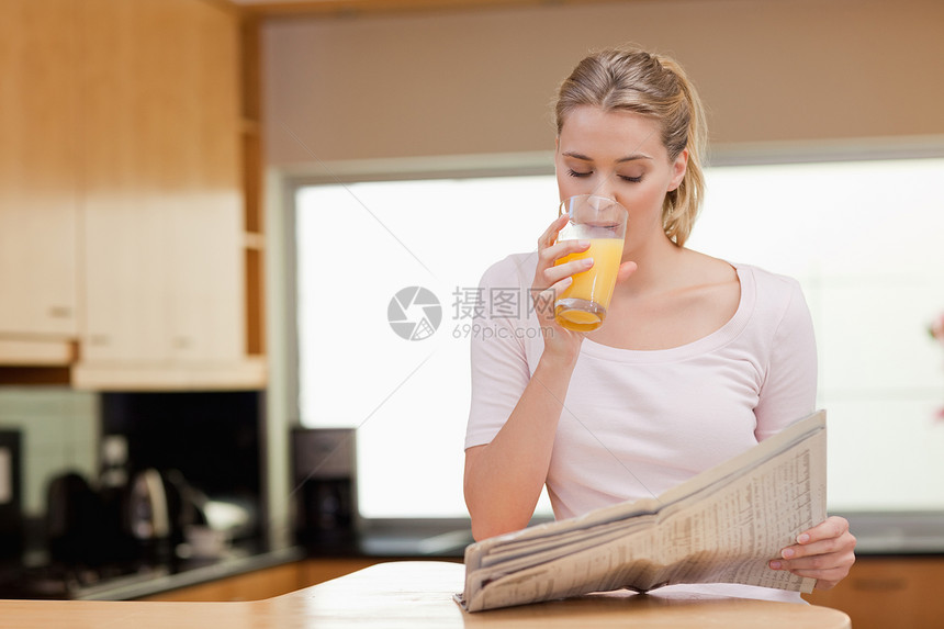 年青女子在喝橙汁时看新闻图片