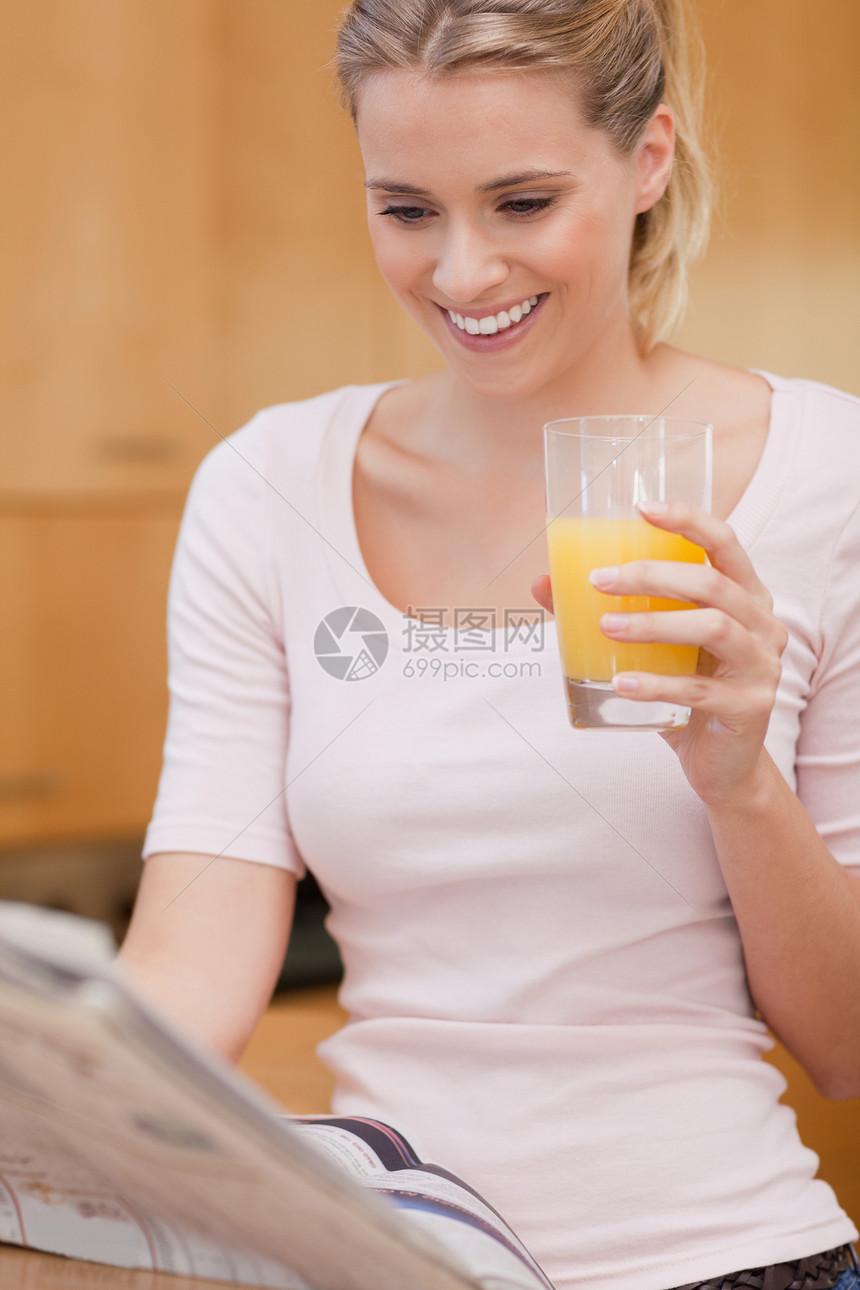 一位年轻女子在喝果汁时看新闻的肖像图片
