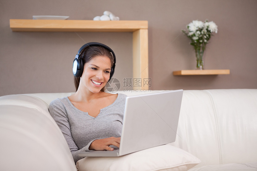 带着耳机和笔记本电脑在沙发上微笑的女人图片