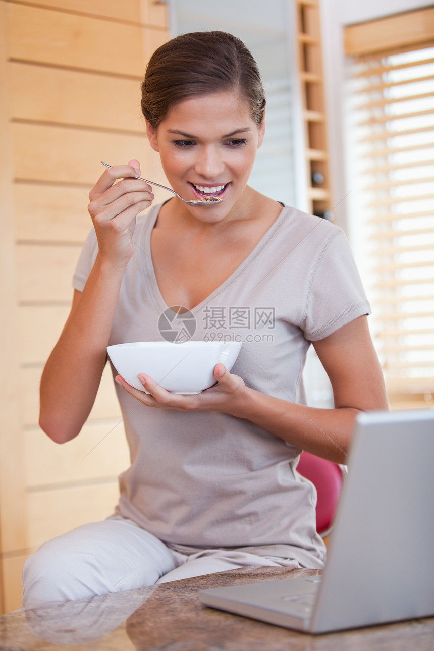 女人在笔记本电脑旁边吃谷物图片