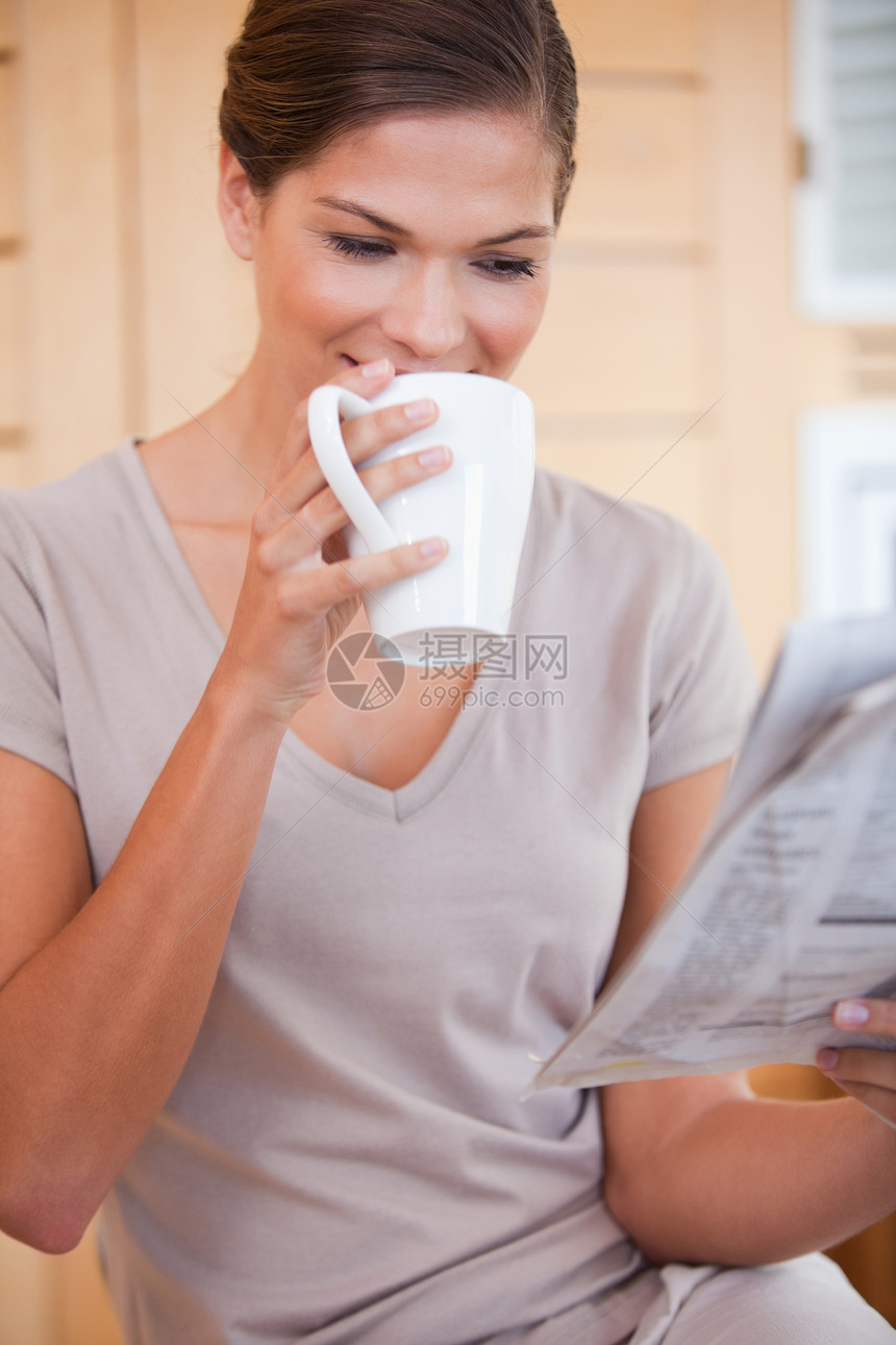 女人在看报纸时喝一小口咖啡图片