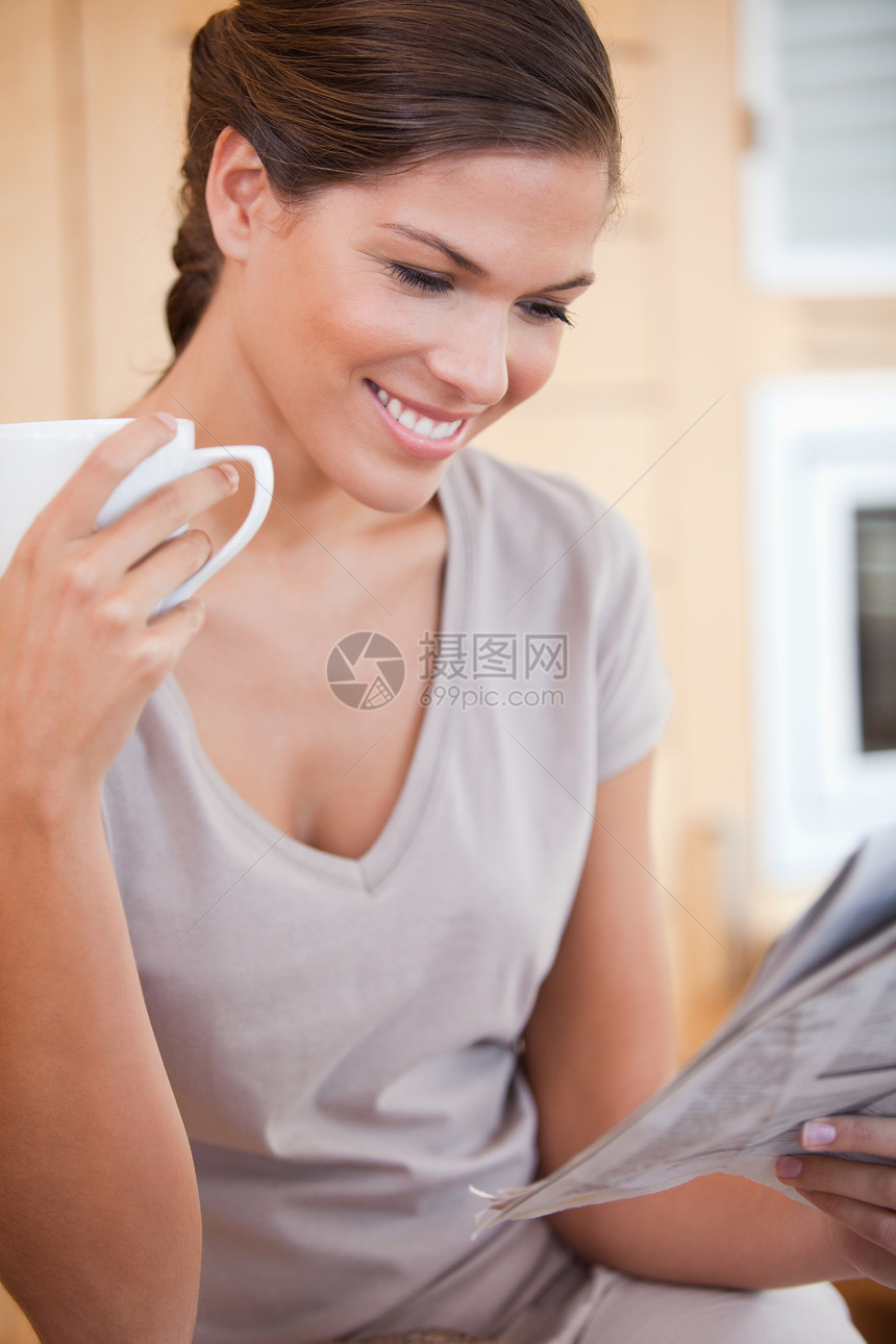 微笑的妇女边喝茶边看报纸;图片