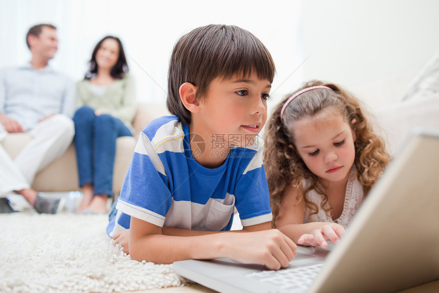 孩子们在地毯上用笔记本电脑 父母在他们身后图片