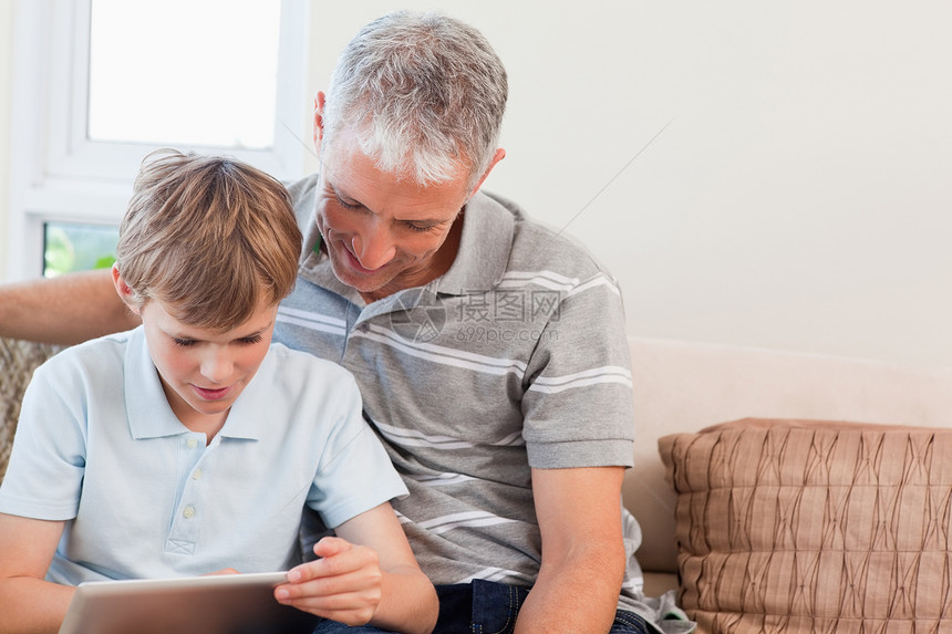 父亲和儿子用平板电脑沙发家长学习客厅药片微笑长椅教育童年男人图片