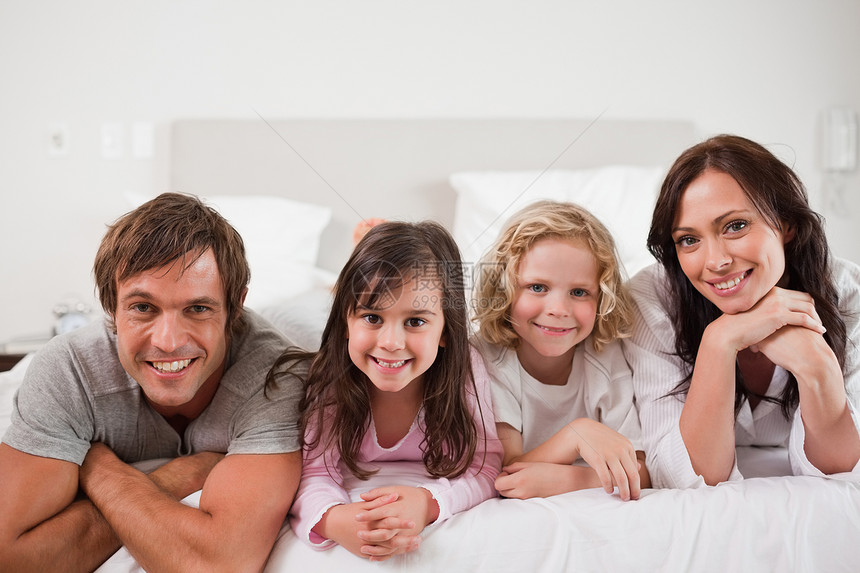 幸福的一家人躺在床上说谎拥抱父亲喜悦享受女儿妻子家长生活乐趣图片