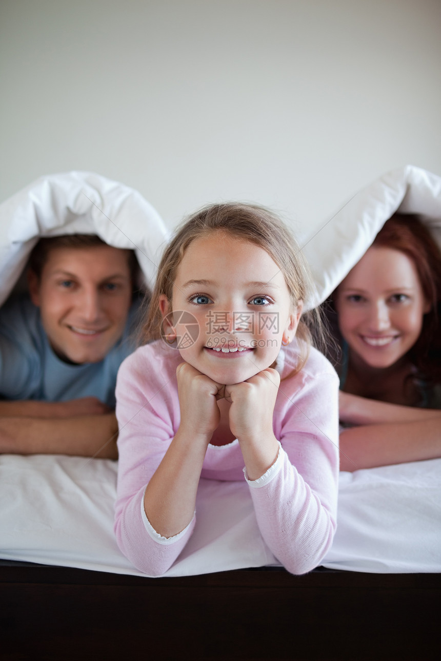 与父母在床罩下微笑的女孩图片