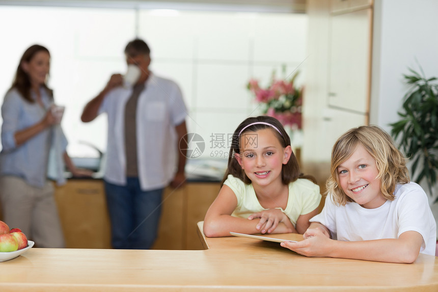 兄弟姐妹在厨房使用平板板电脑 父母在厨房后面图片